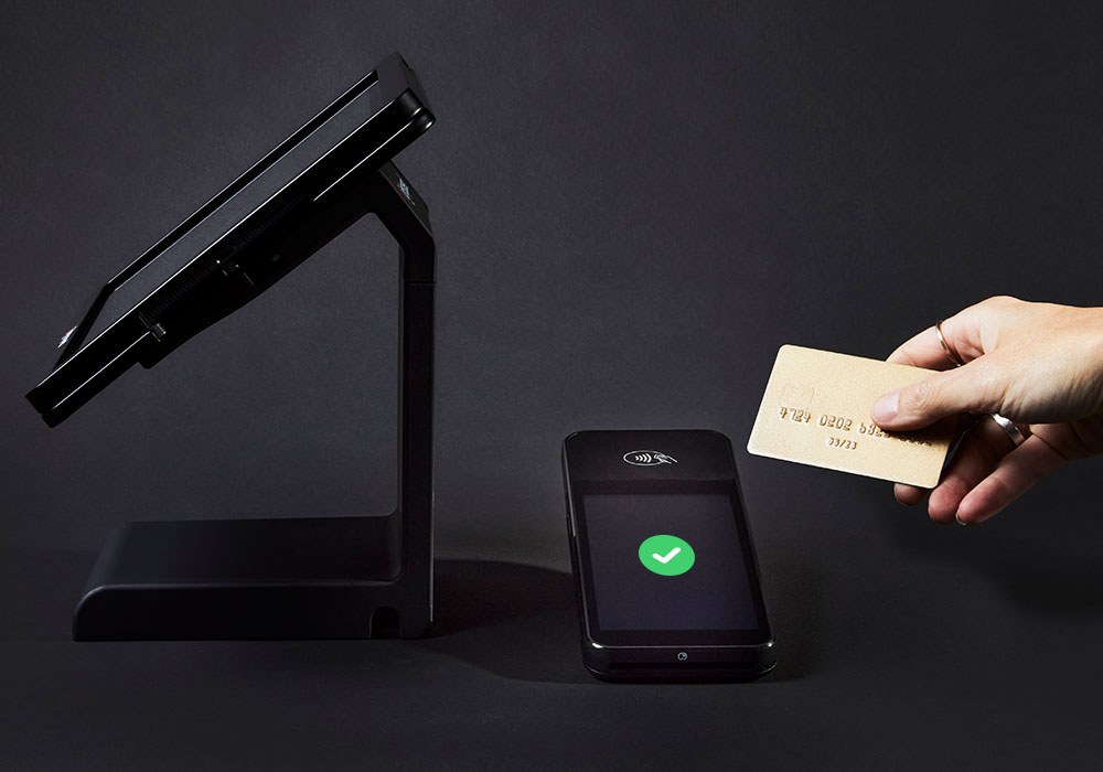 Side view of Lightspeed Retail in an iPad stand, hand is making contactless payment on the right.