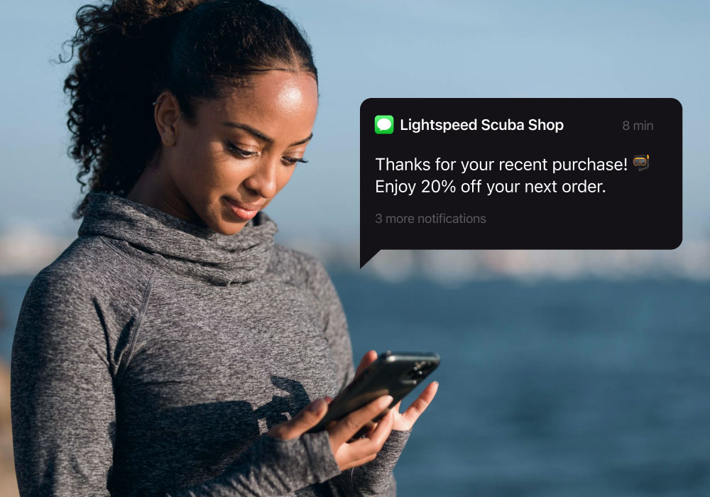 A woman looks at her phone with a floating module showing a text sent from Lightspeed's scuba store POS.
