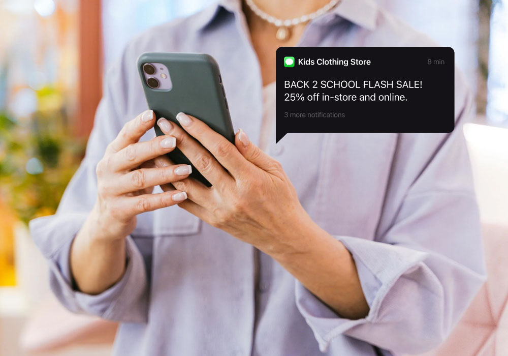 A woman looks at a cell phone with a text message that shows an online store sale.
