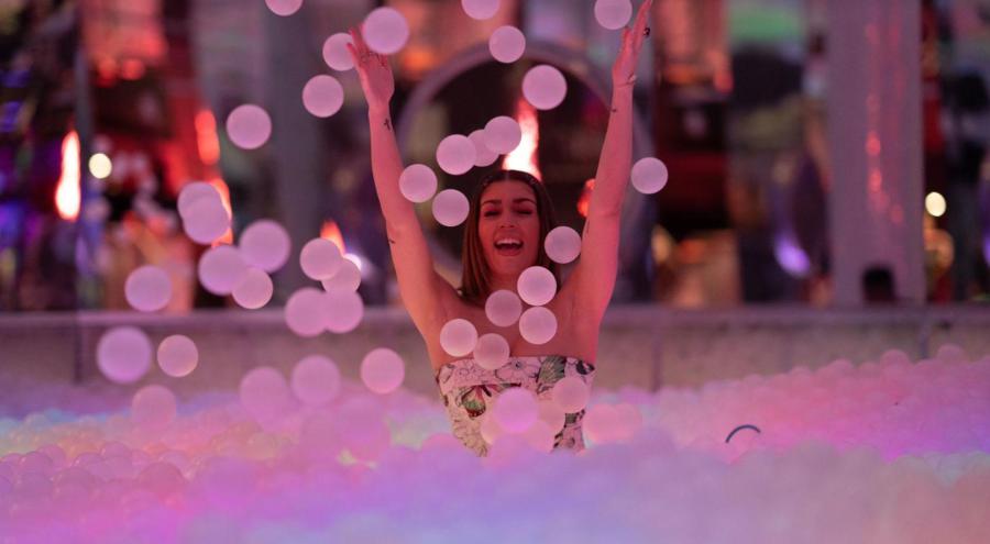 Person playing in ballpit, throwing plastic balls in the air with pink and blue background