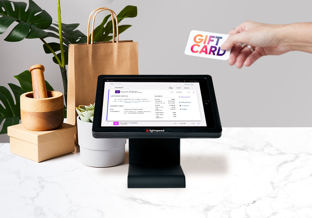 Hand holding a gift card reaching toward an iPad ePOS