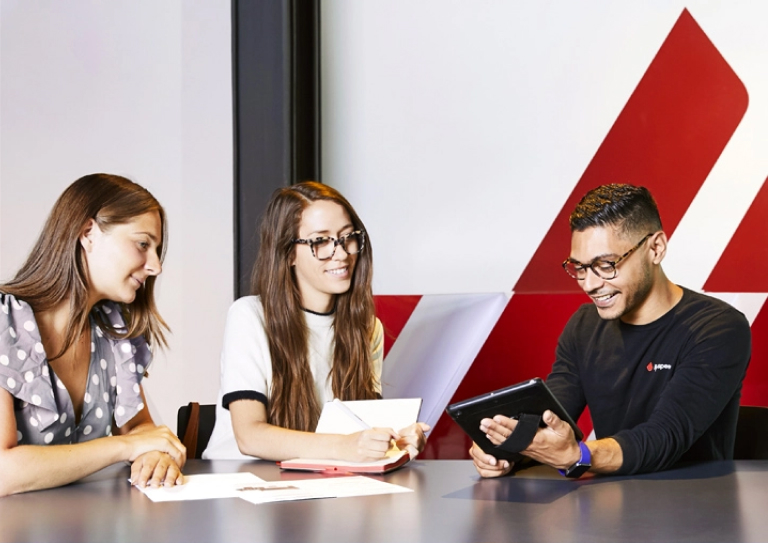 Three people sat smiling, one of them is holding an iPad and the others are looking at it