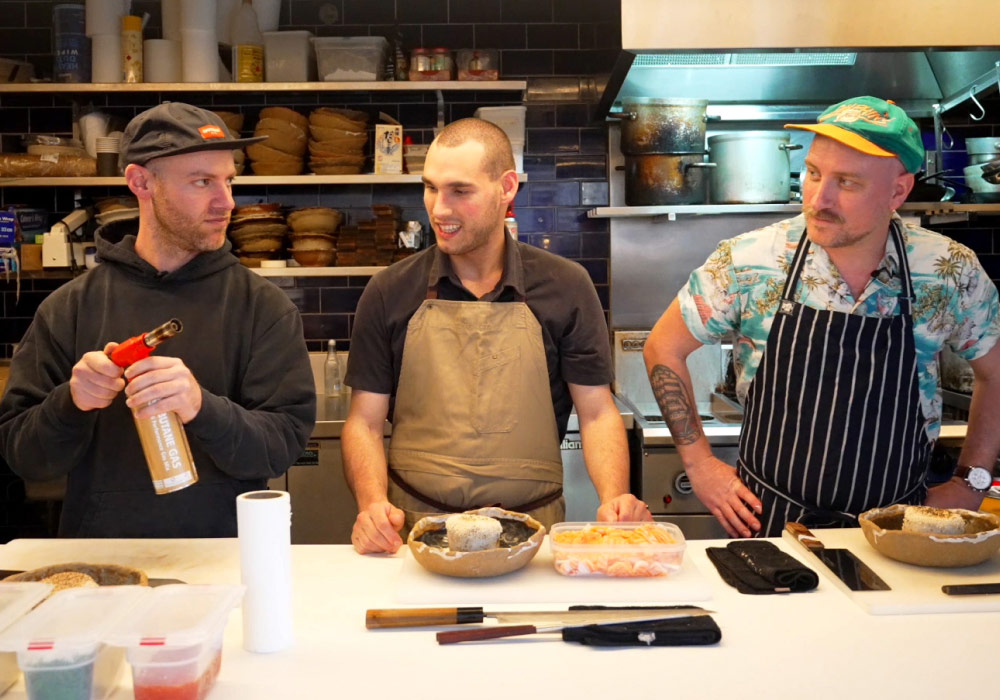 3 chefs chatting in TenTo's kitchen, one holding a blowtorch