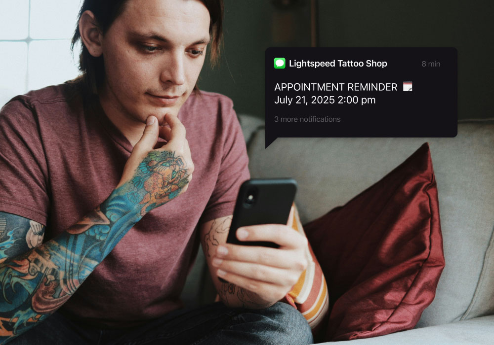 A tattooed individual looking at their phone with a floating module that shows a text from a Lightspeed business using a tattoo shop pos
