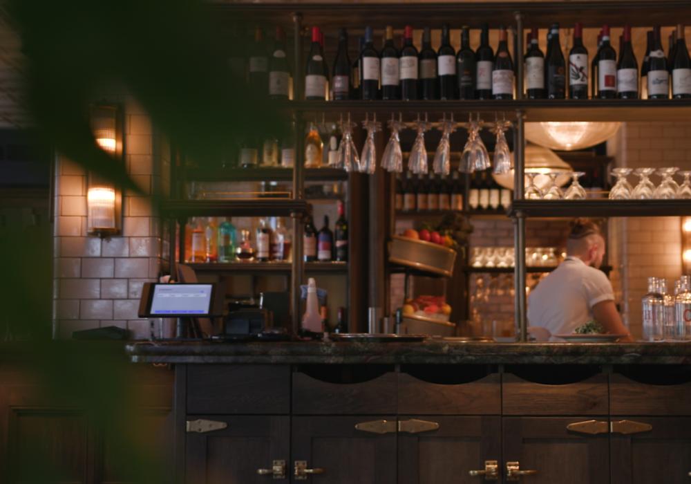 A pub with someone working behind the bar with bottles and glasses in the front of the bar