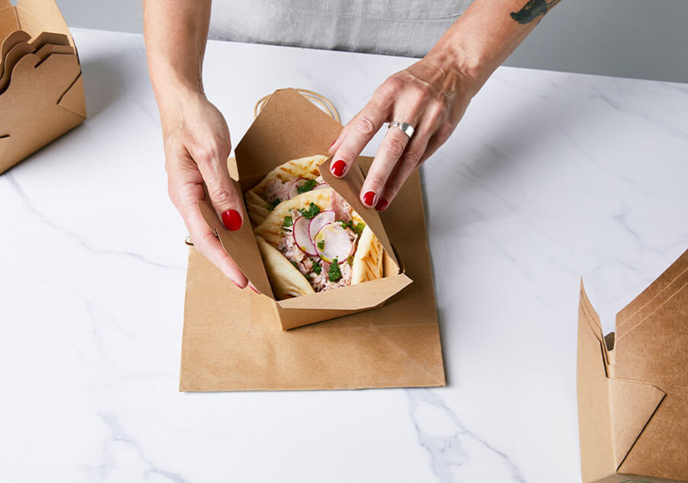 A marble table with someone closing a takeaway box filled with flatbreads