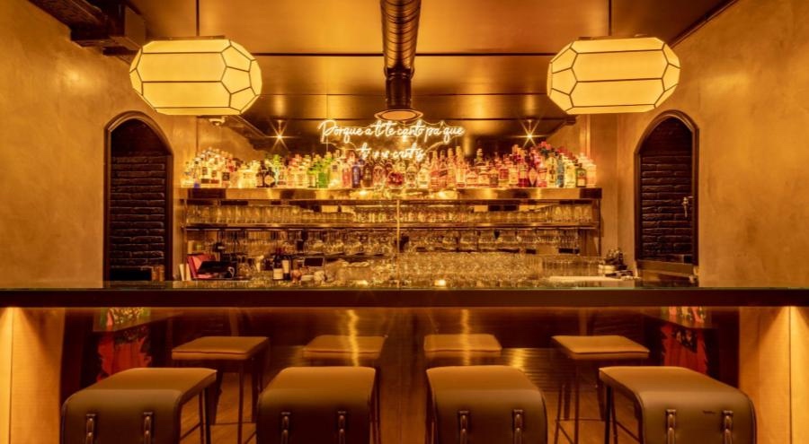 A bar with warm amber lighting with high bar stools and bottles behind the bar