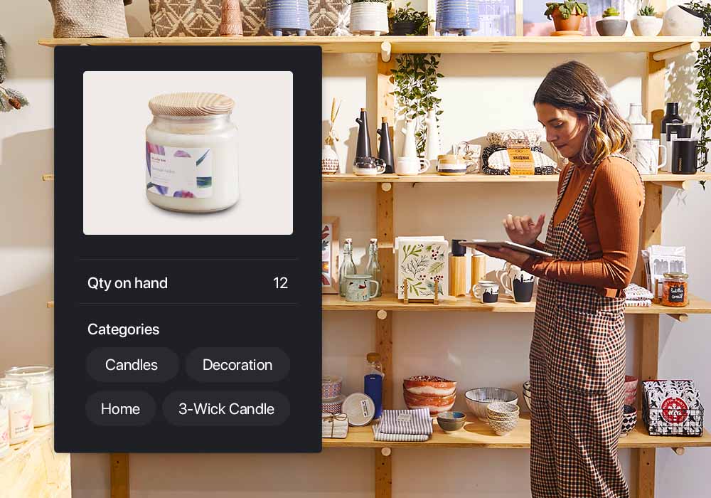 Scented candle shown on Lightspeed Retail's inventory management interface. Quantity on hand, re-order point and product categories are shown below it. Retailer using iPad in shop in background.