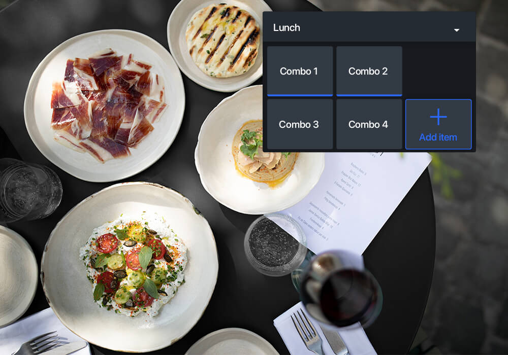 An overhead shot of a black table laid with plates and bowls of food including jamon, flatbreads and tomatoes
