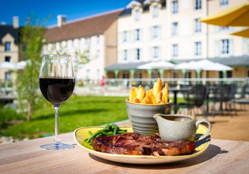 A table outside laid with a plate of steak and chips, with a glass of red wine in the background