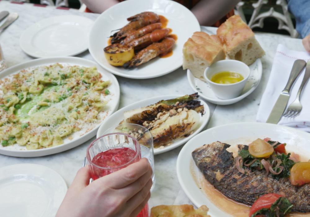 A marble table topped with plates of orecchiette, focaccia, grilled hispi cabbage and prawns